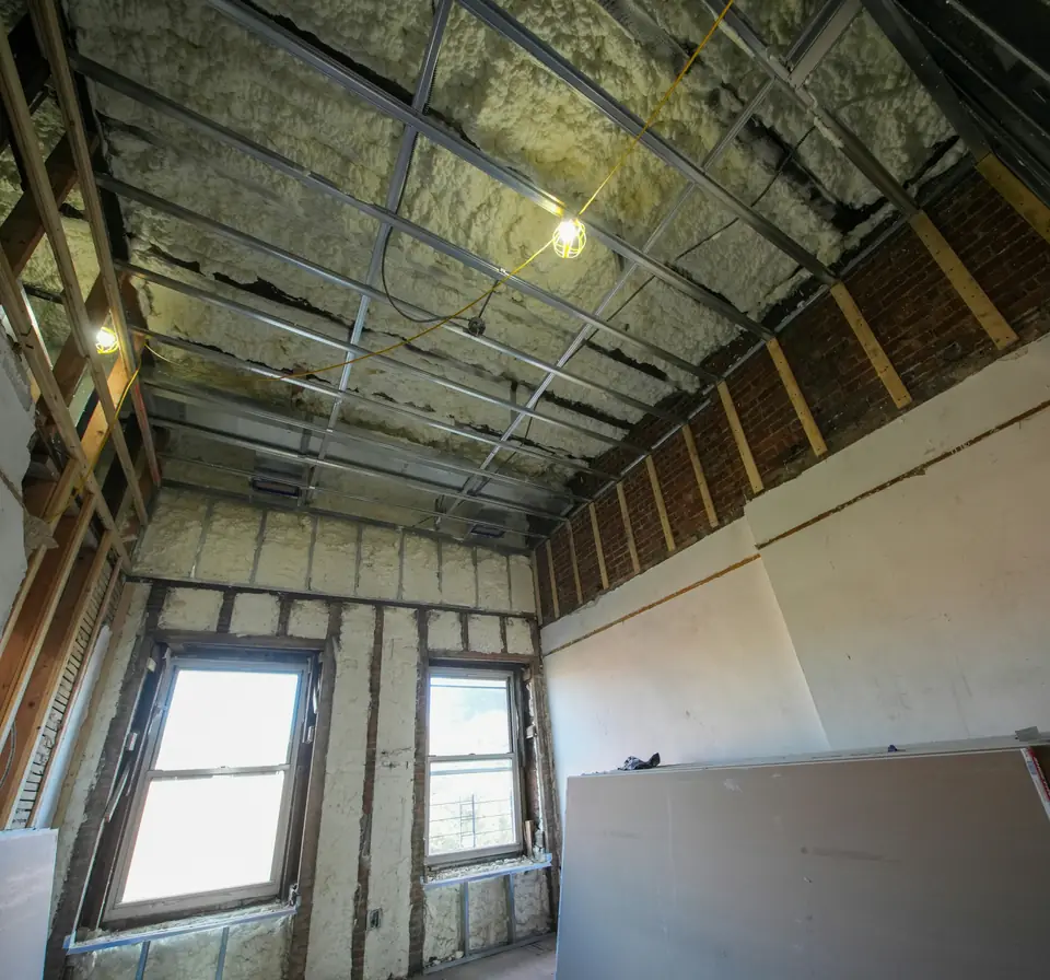 A gutted top-floor room with cured spray foam filling the walls and ceiling around the windows
